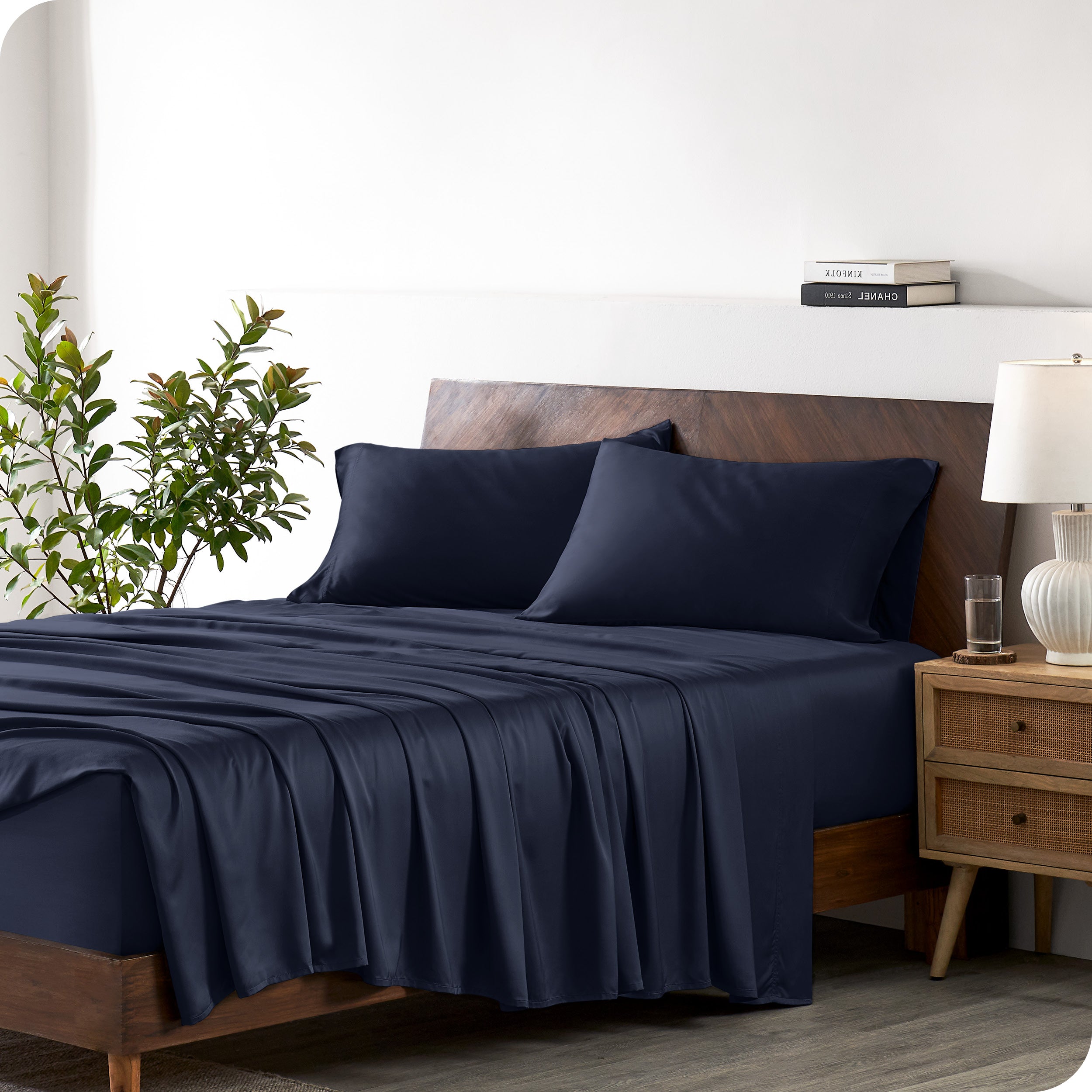 Modern bedroom with a bed against a white wall with a nightstand next to the bed. The bed has bamboo sheets draped over it.