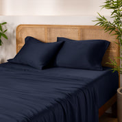 Bamboo bed sheets and pillowcases on a bed with a wicker headboard and plants in the background.