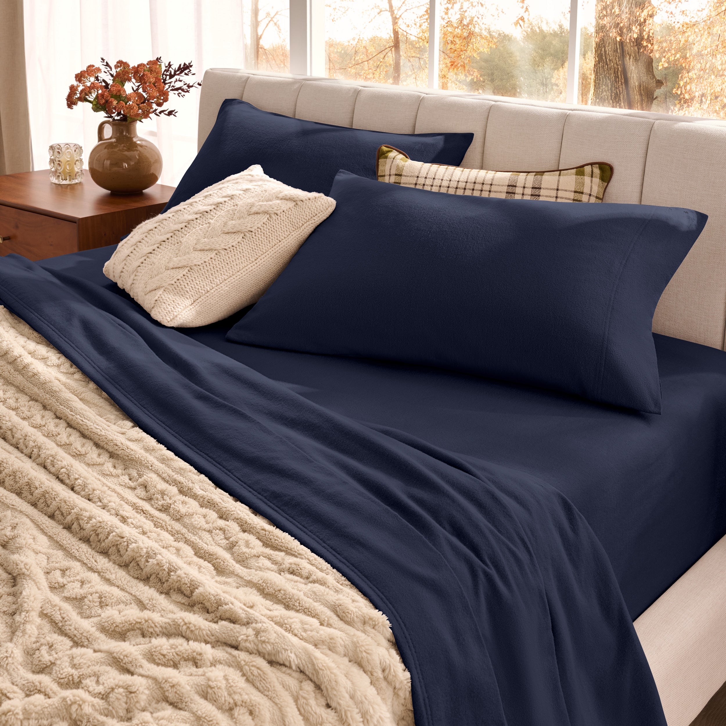 Neatly made bed with pillows and a beige blanket in a bright room.