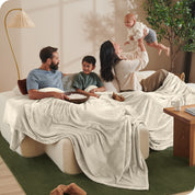 A family sitting on a couch with a giant microplush blanket covering them