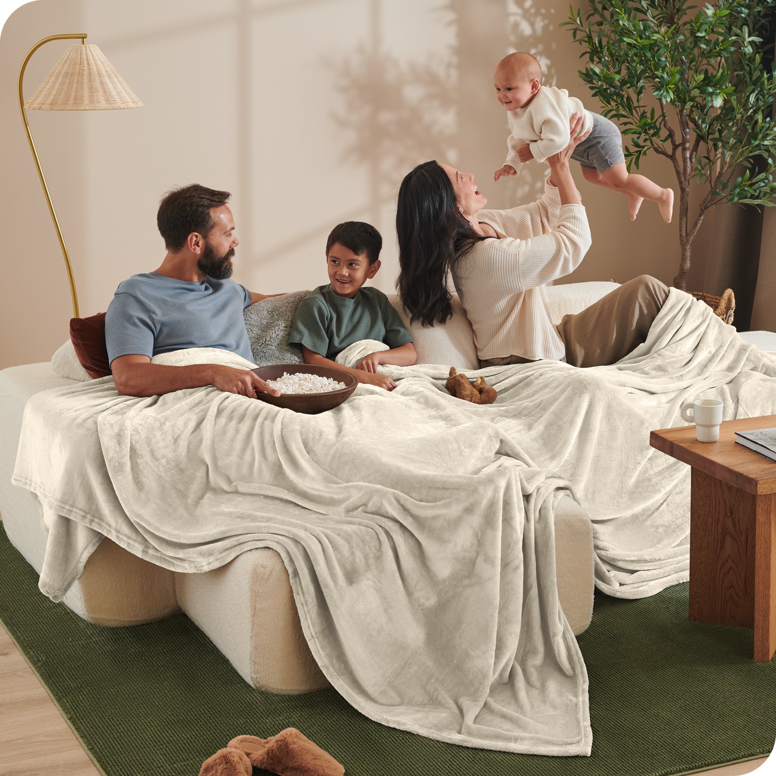 A family sitting on a couch with a giant microplush blanket covering them