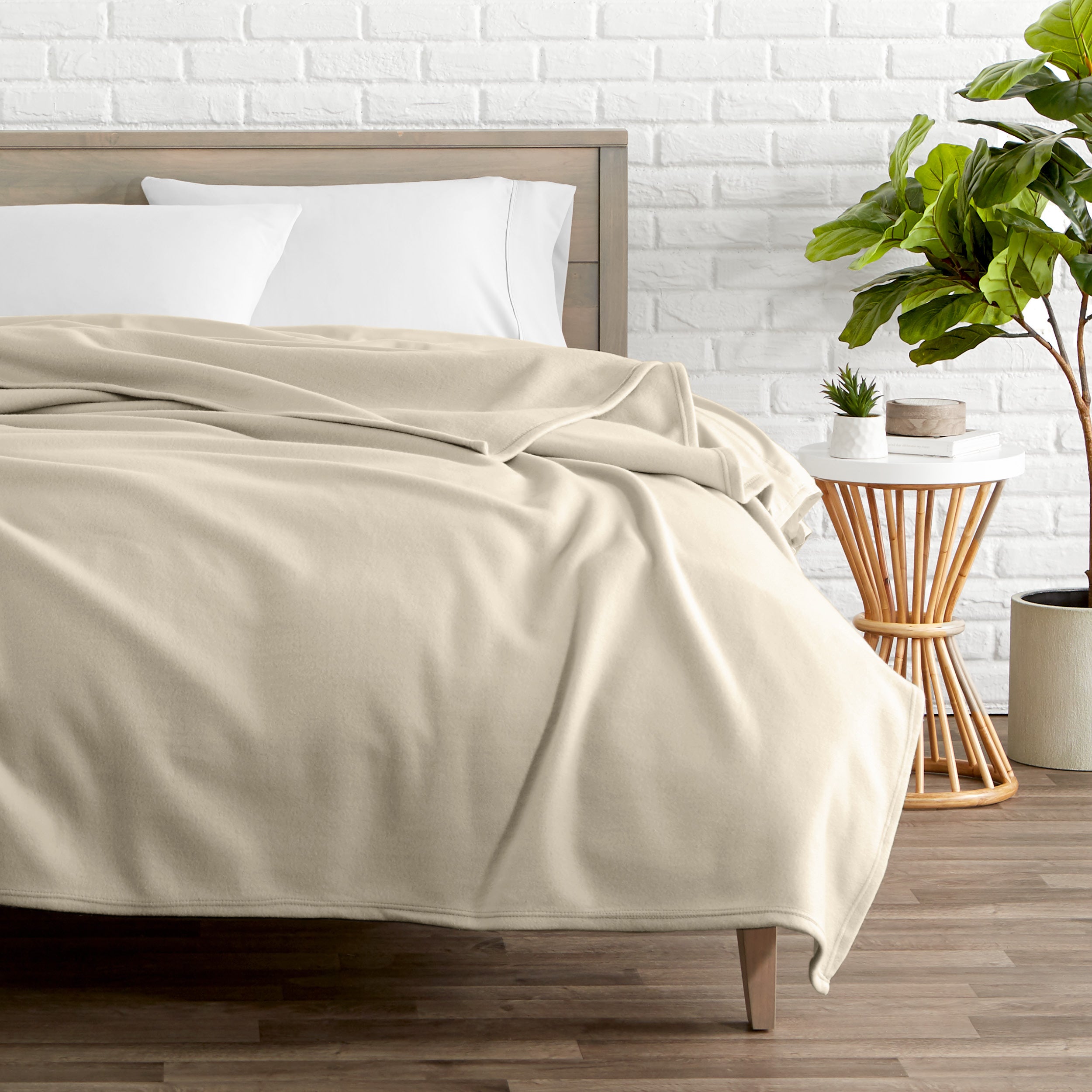 A polar fleece blanket on a bed next to a table and a large plant