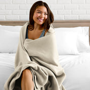 A woman sitting at the end of a bed with a fleece blanket wrapped around her shoulders