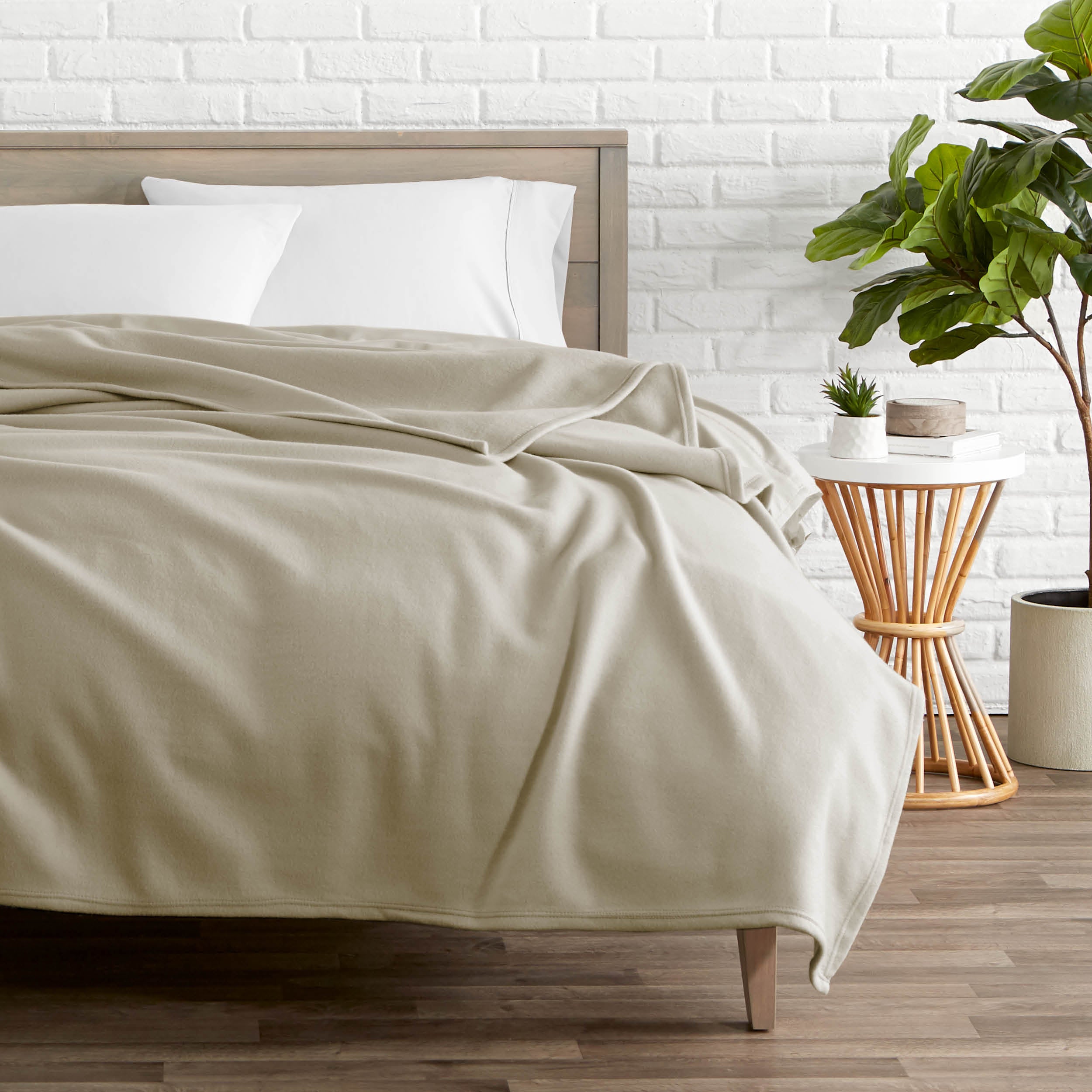 A polar fleece blanket on a bed next to a table and a large plant