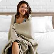 A woman sitting at the end of a bed with a fleece blanket wrapped around her shoulders