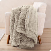 A woman sitting on the end of a bed with a shaggy blanket wrapped around her