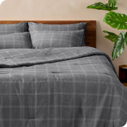 Gray plaid bedding set on a bed with a wooden headboard and plants in the background.