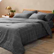 Gray plaid bedding set on a bed in a bedroom setting with a lamp and plant.