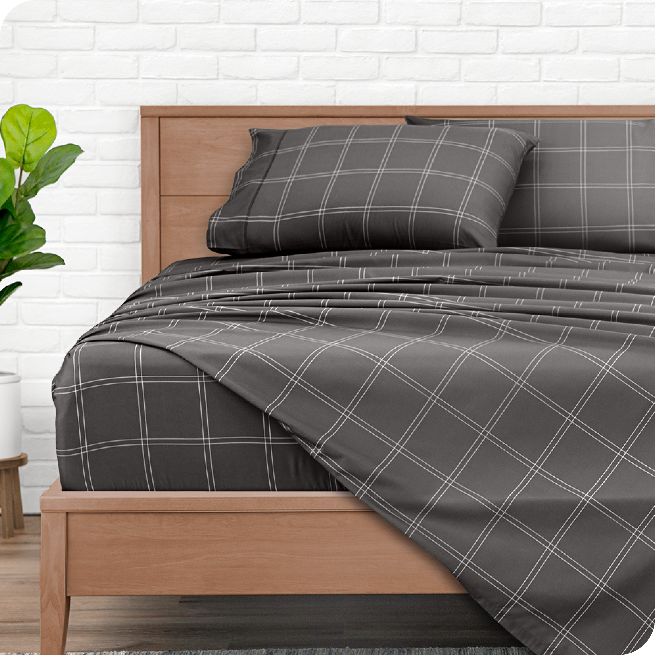 Gray plaid sheet set on a wooden bed with a white brick wall background