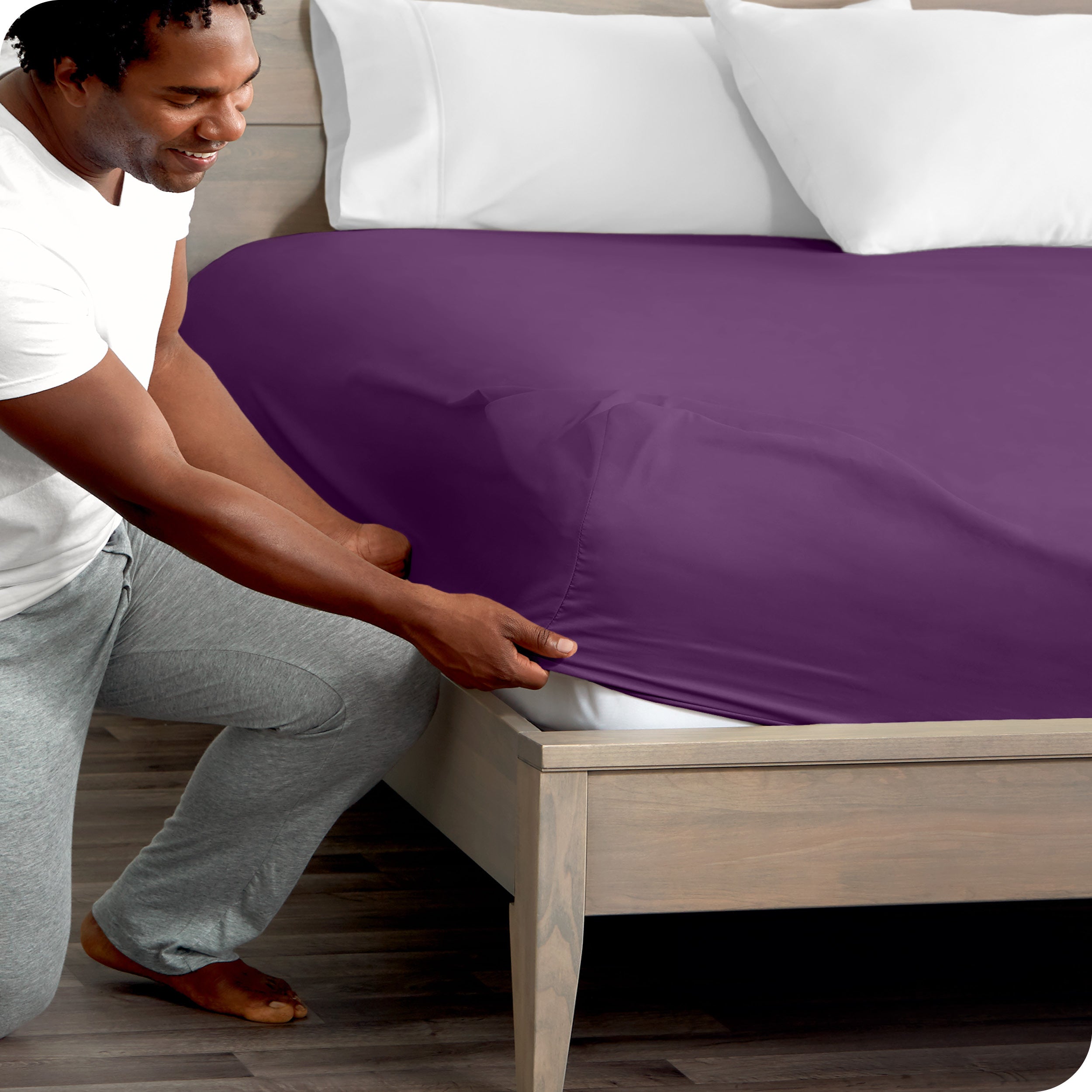A man kneeling while putting a fitted sheet on a bed