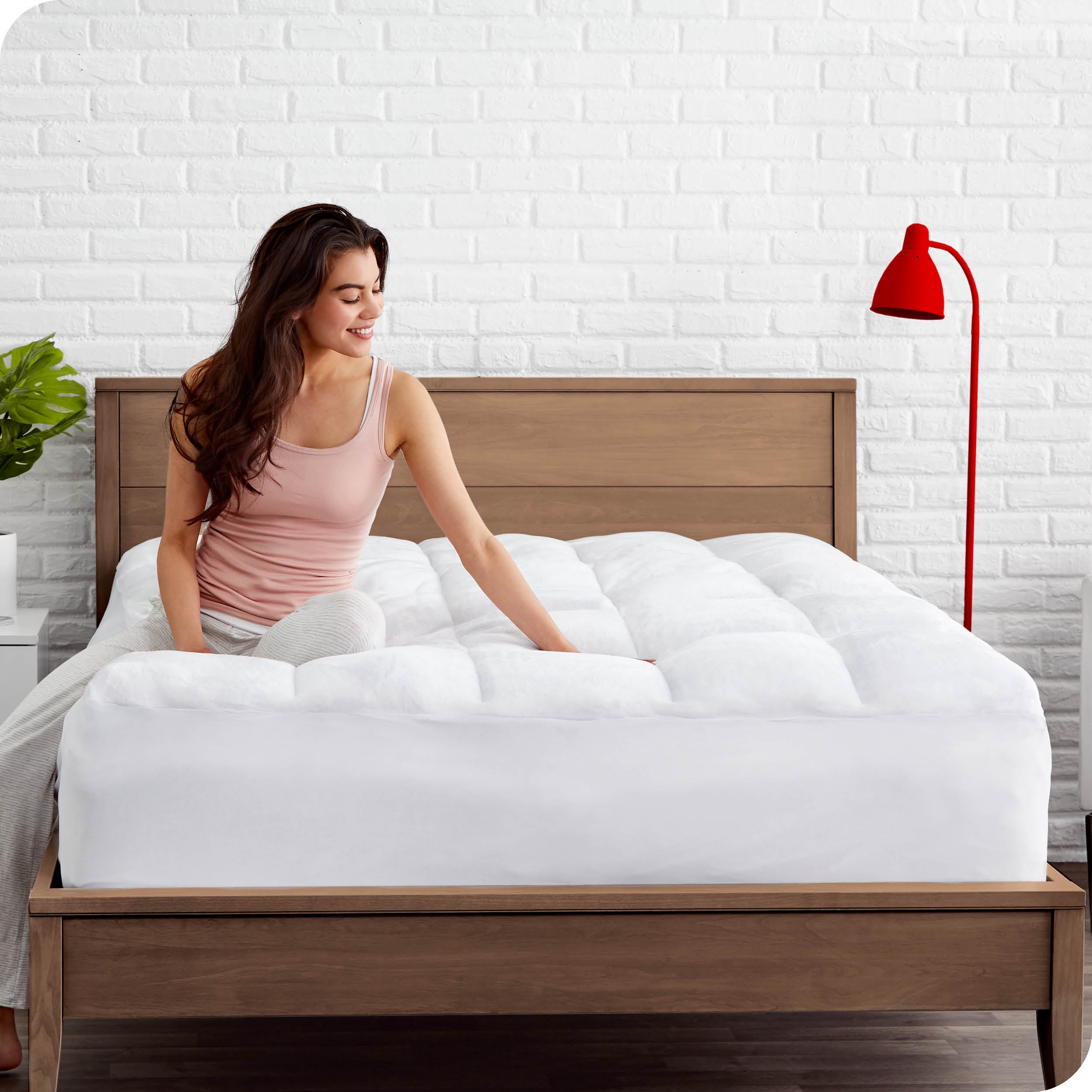 A woman is sitting on a bed with a mattress pad on it.