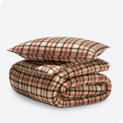 A folded stack of a printed flannel duvet cover with one pillows on top.
