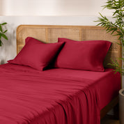 Bamboo bed sheets and pillowcases on a bed with a wicker headboard and plants in the background.
