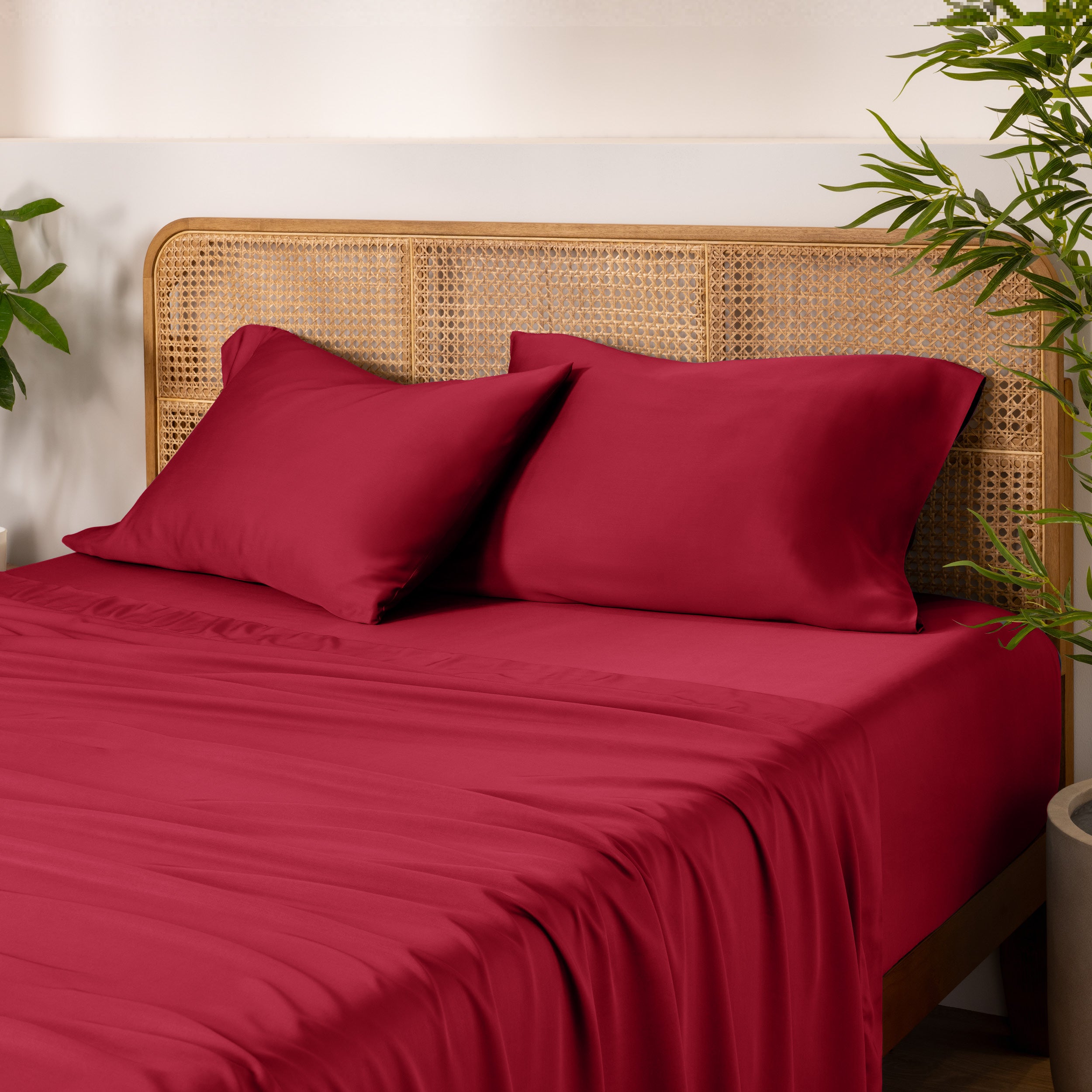 Bamboo bed sheets and pillowcases on a bed with a wicker headboard and plants in the background.
