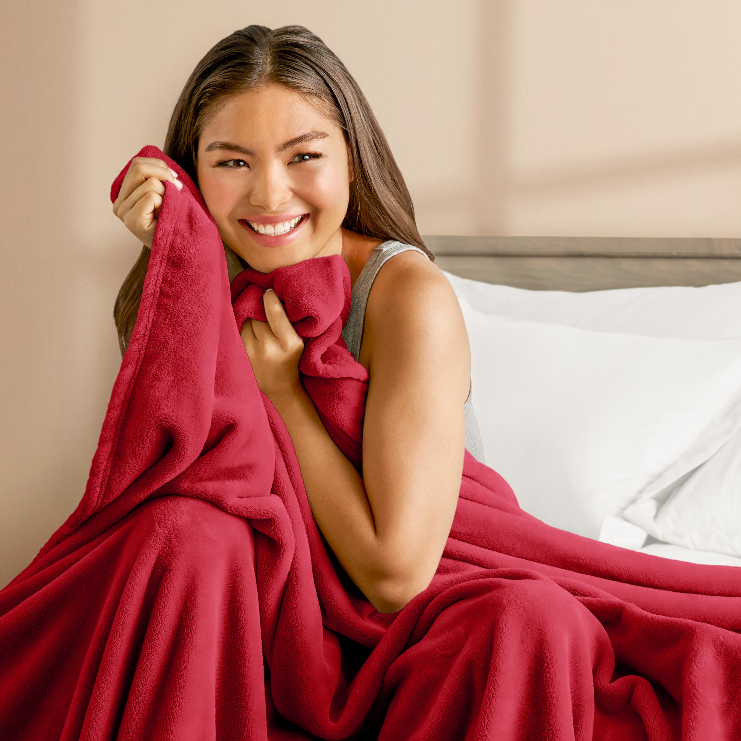 A woman sitting on a bed wrapped in a microplush blanket
