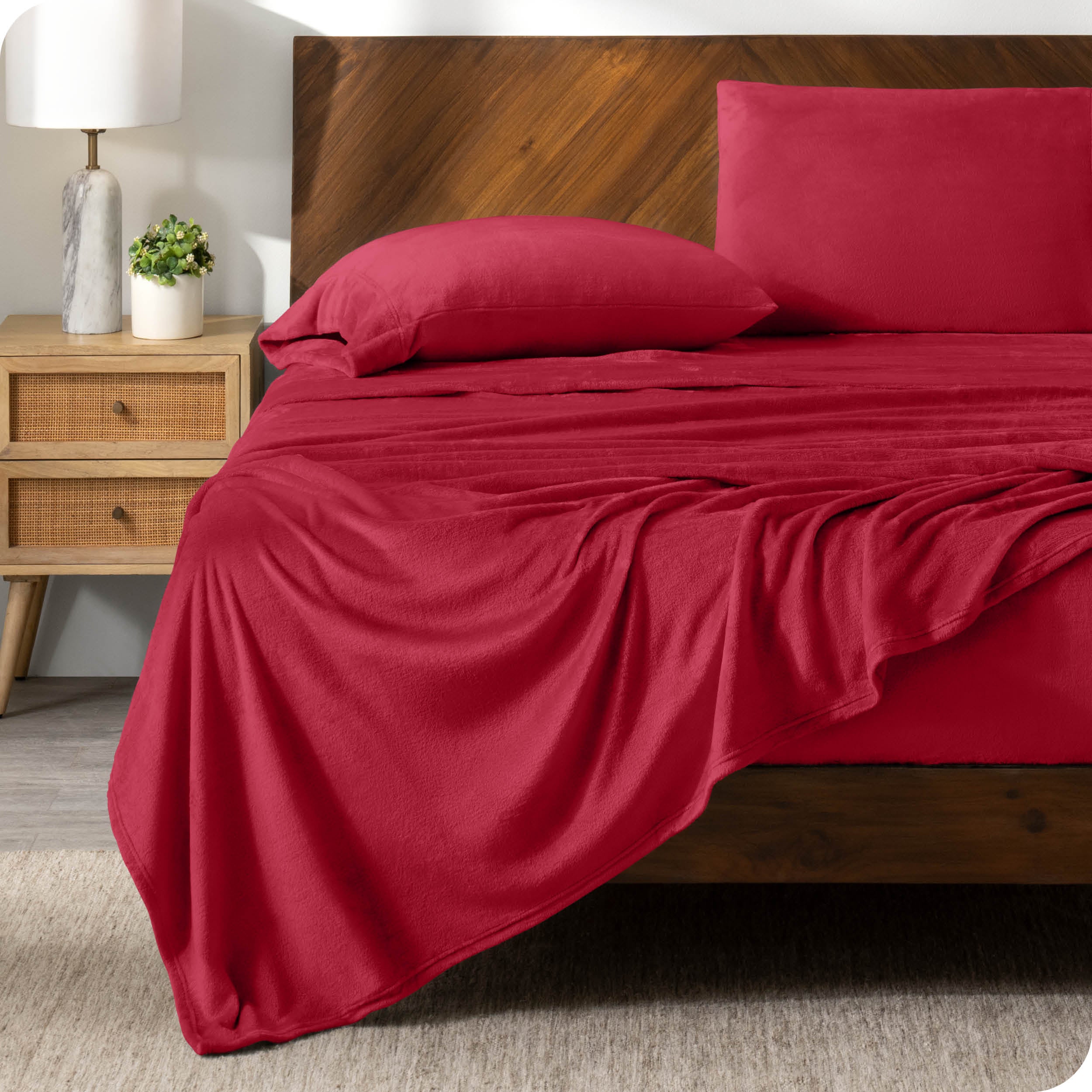 A red sheet set on a bed with a wooden bed frame