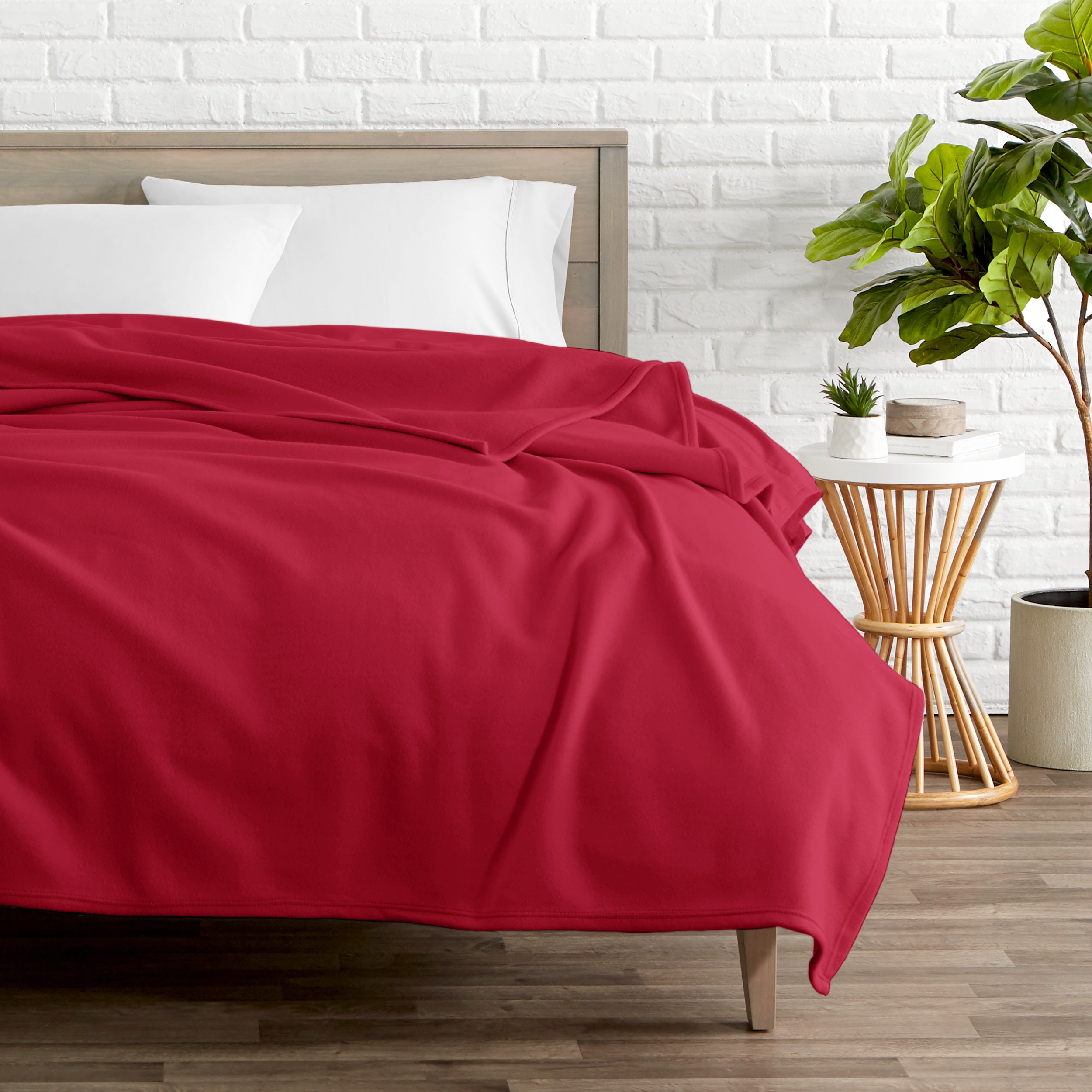 A polar fleece blanket on a bed next to a table and a large plant
