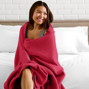 A woman sitting at the end of a bed with a fleece blanket wrapped around her shoulders