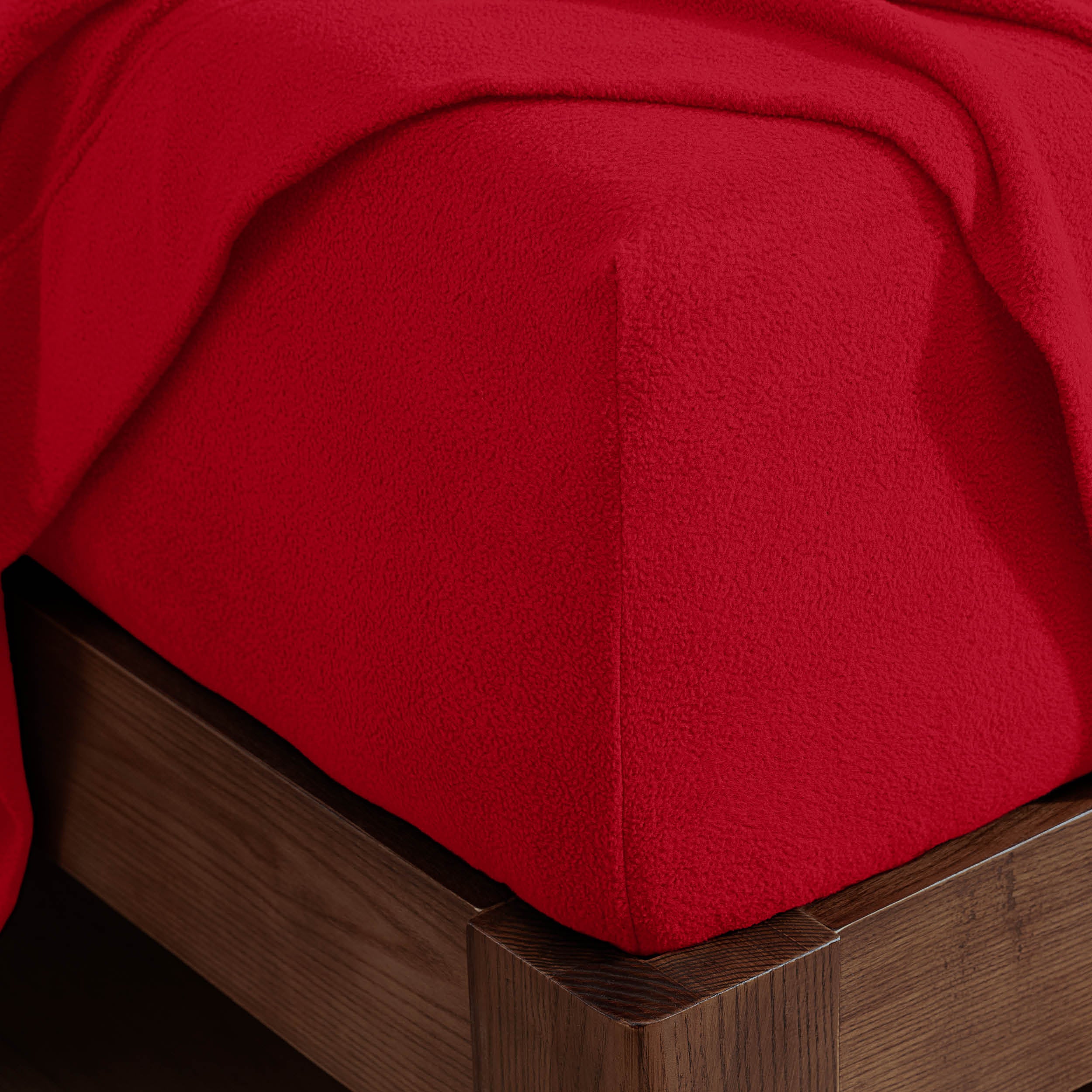 Corner of the bed with a fitted sheet on the mattress and a flat sheet draped over the side and end