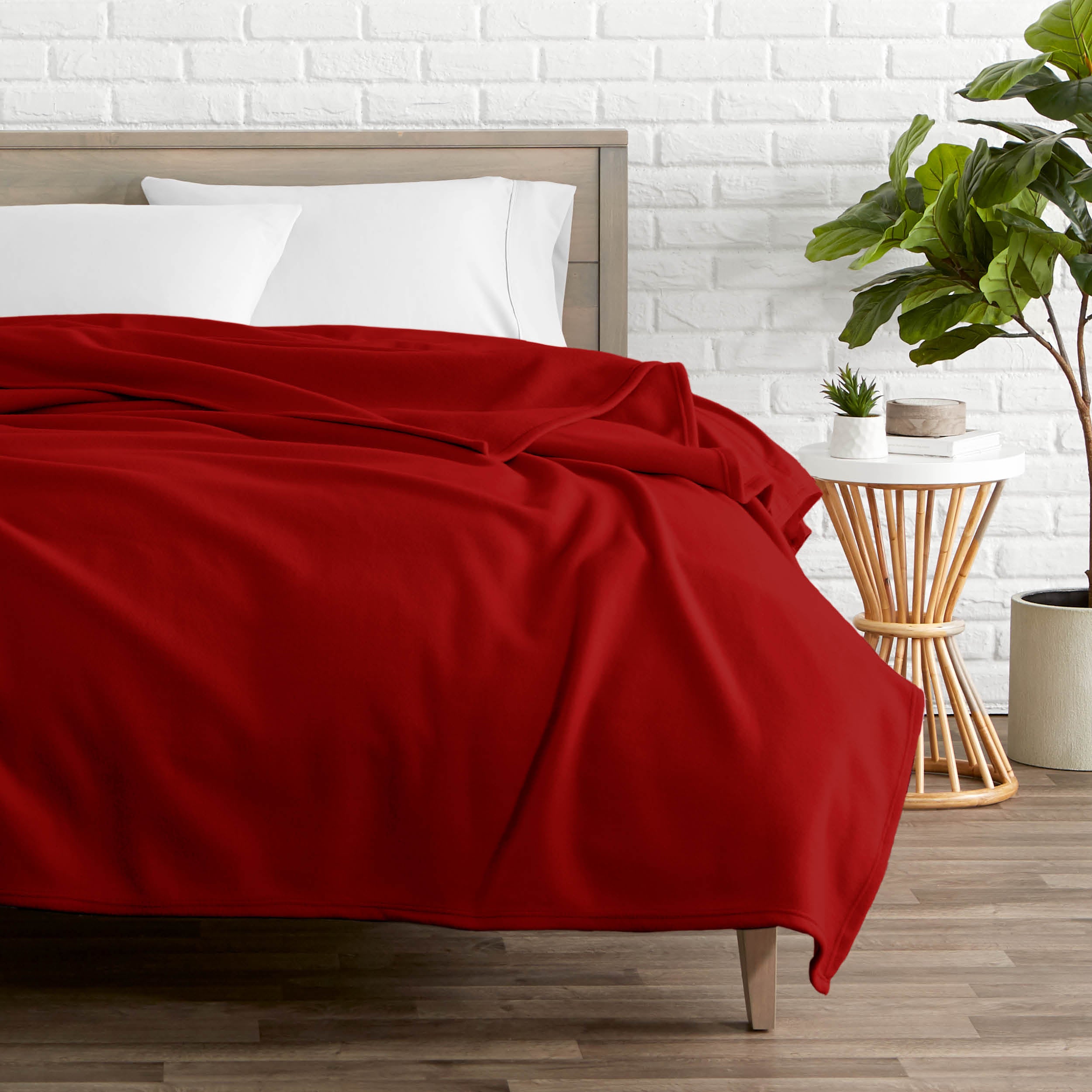 A polar fleece blanket on a bed next to a table and a large plant