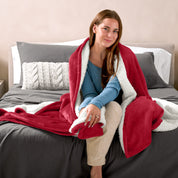 Woman cuddling with a sherpa blanket while sitting on the end of a bed