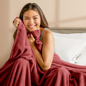 A woman sitting on a bed wrapped in a microplush blanket