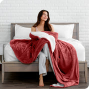 Woman cuddling with a sherpa blanket while sitting on the end of a bed