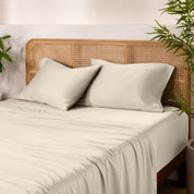 Bamboo bed sheets and pillowcases on a bed with a wicker headboard and plants in the background.