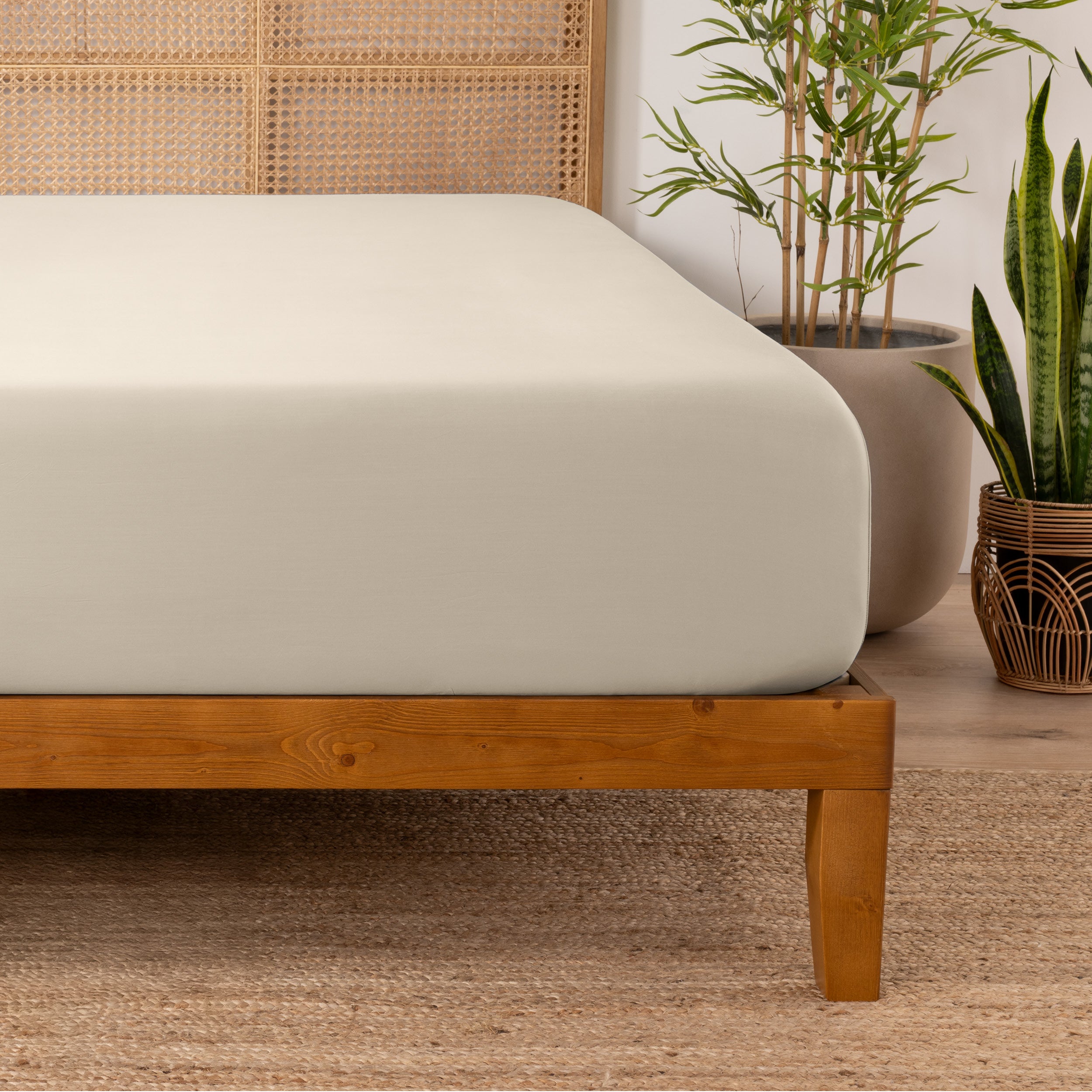 Bamboo fitted sheet on a wooden bed with plants in the background
