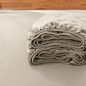 Folded fitted sheet on a bed with a wooden headboard.