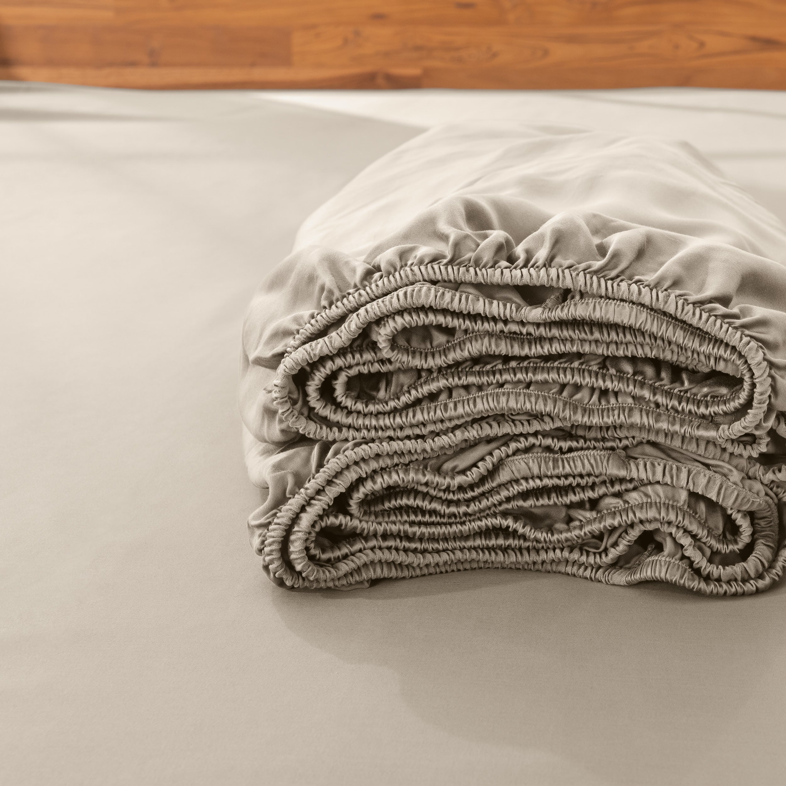 Folded fitted sheet on a bed with a wooden headboard.