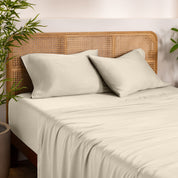 Bamboo bed sheets and pillowcases on a bed with a wicker headboard in a room with plants.