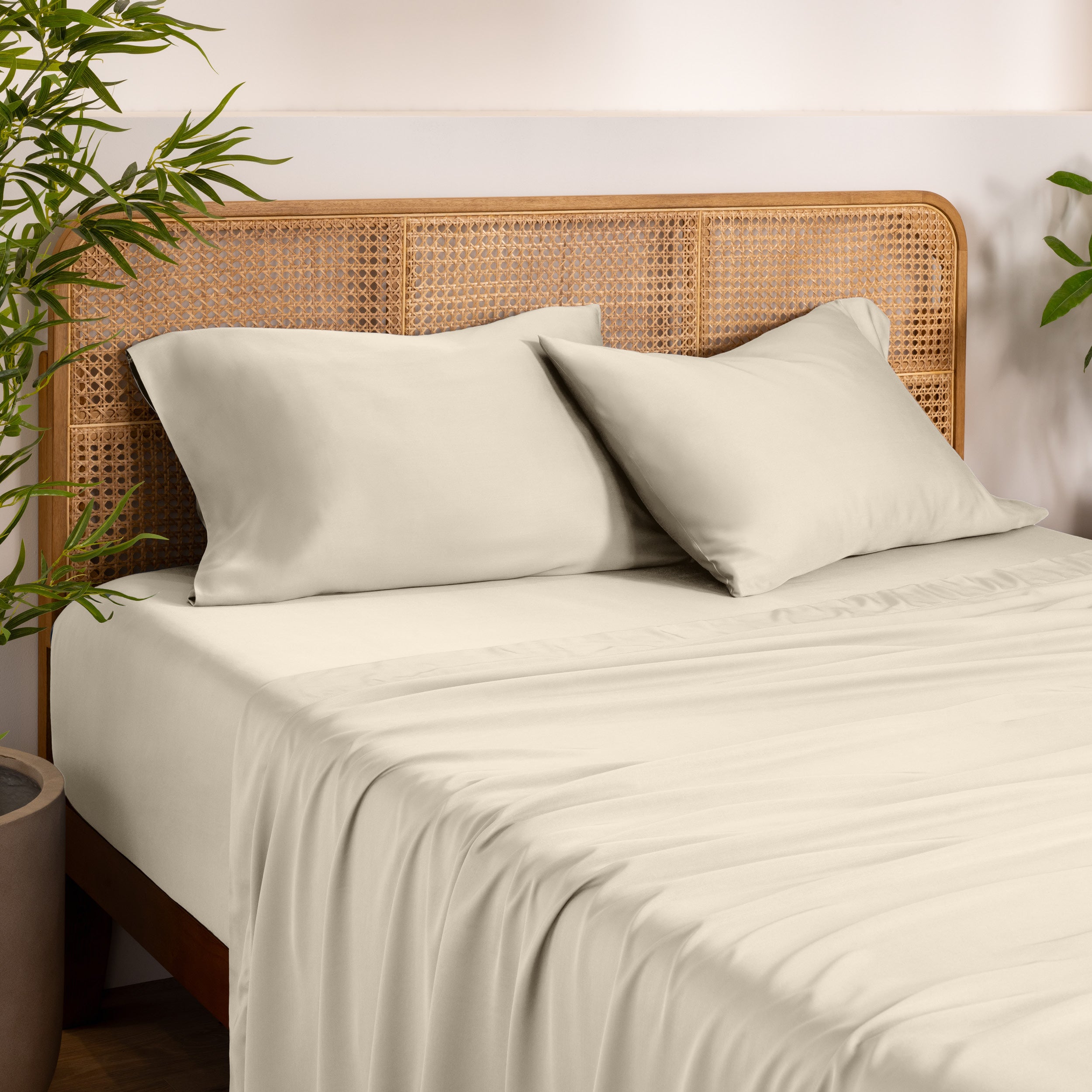 Bamboo bed sheets and pillowcases on a bed with a wicker headboard in a room with plants.