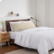 A body pillow cover on a pillow on a bed made with all white bedding