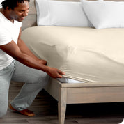 A man kneeling while putting a fitted sheet on a bed