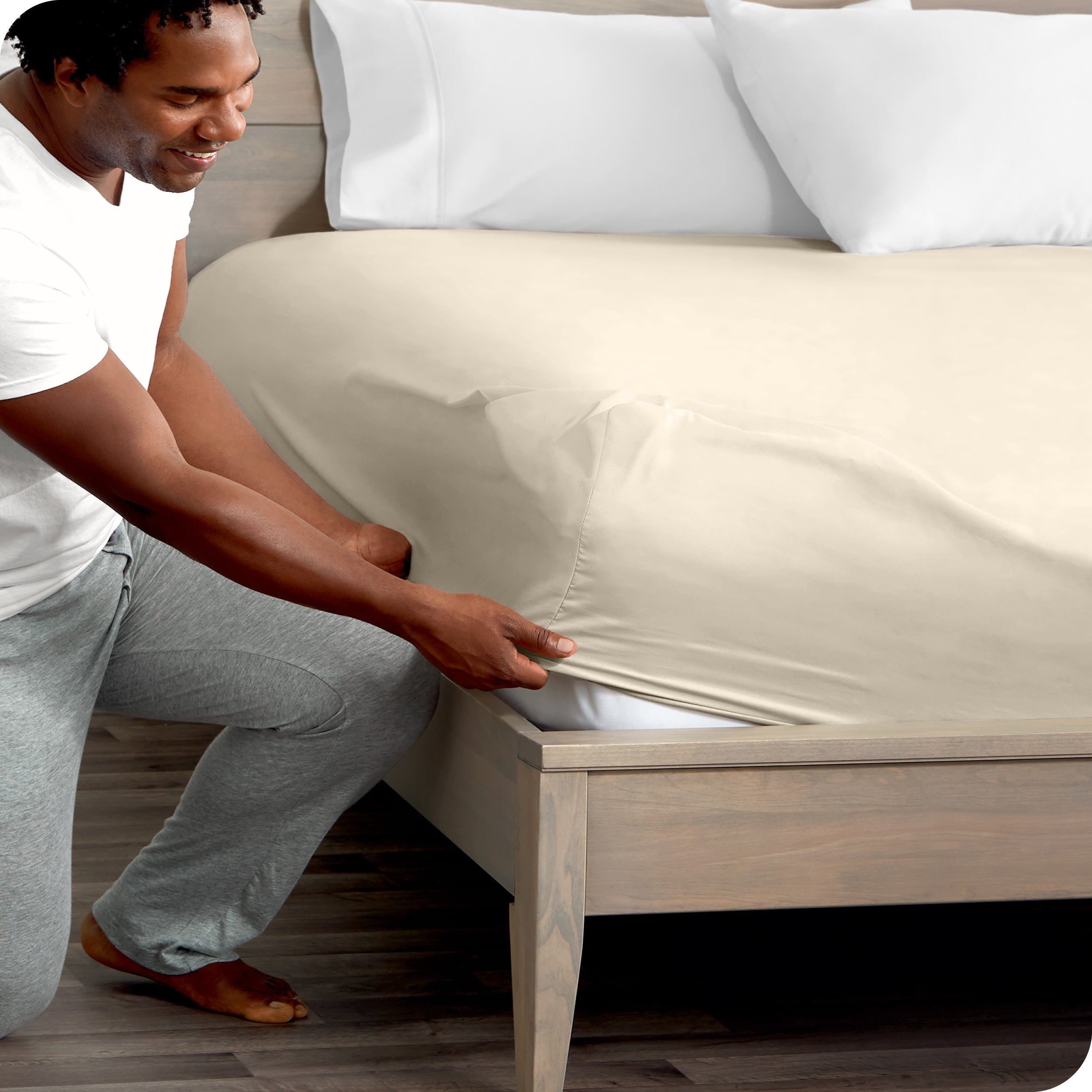 A man kneeling while putting a fitted sheet on a bed