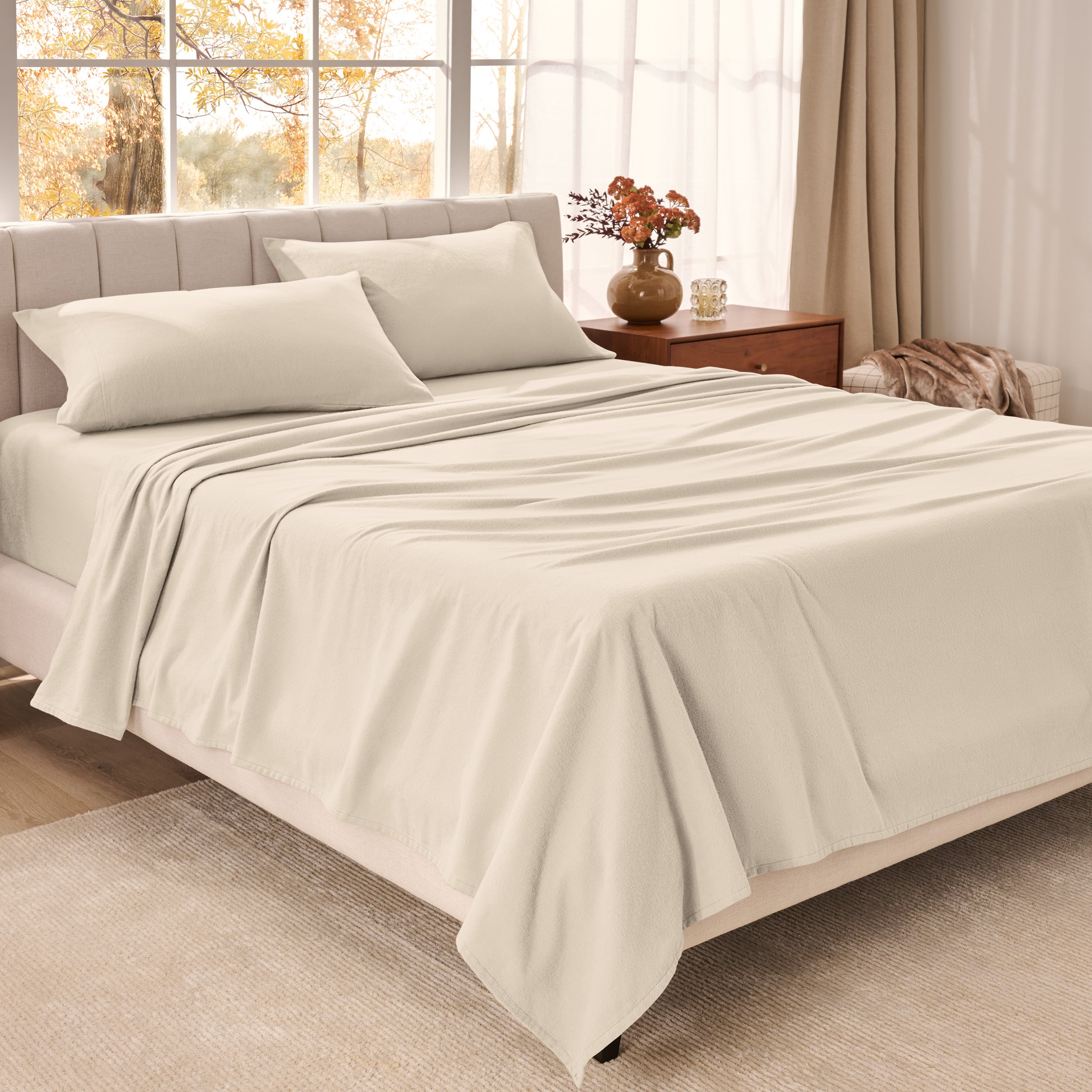 Organic flannel bed sheets on a neatly made bed in a bright bedroom with large windows.