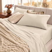 Neatly made bed with pillows and a beige blanket in a bright room.