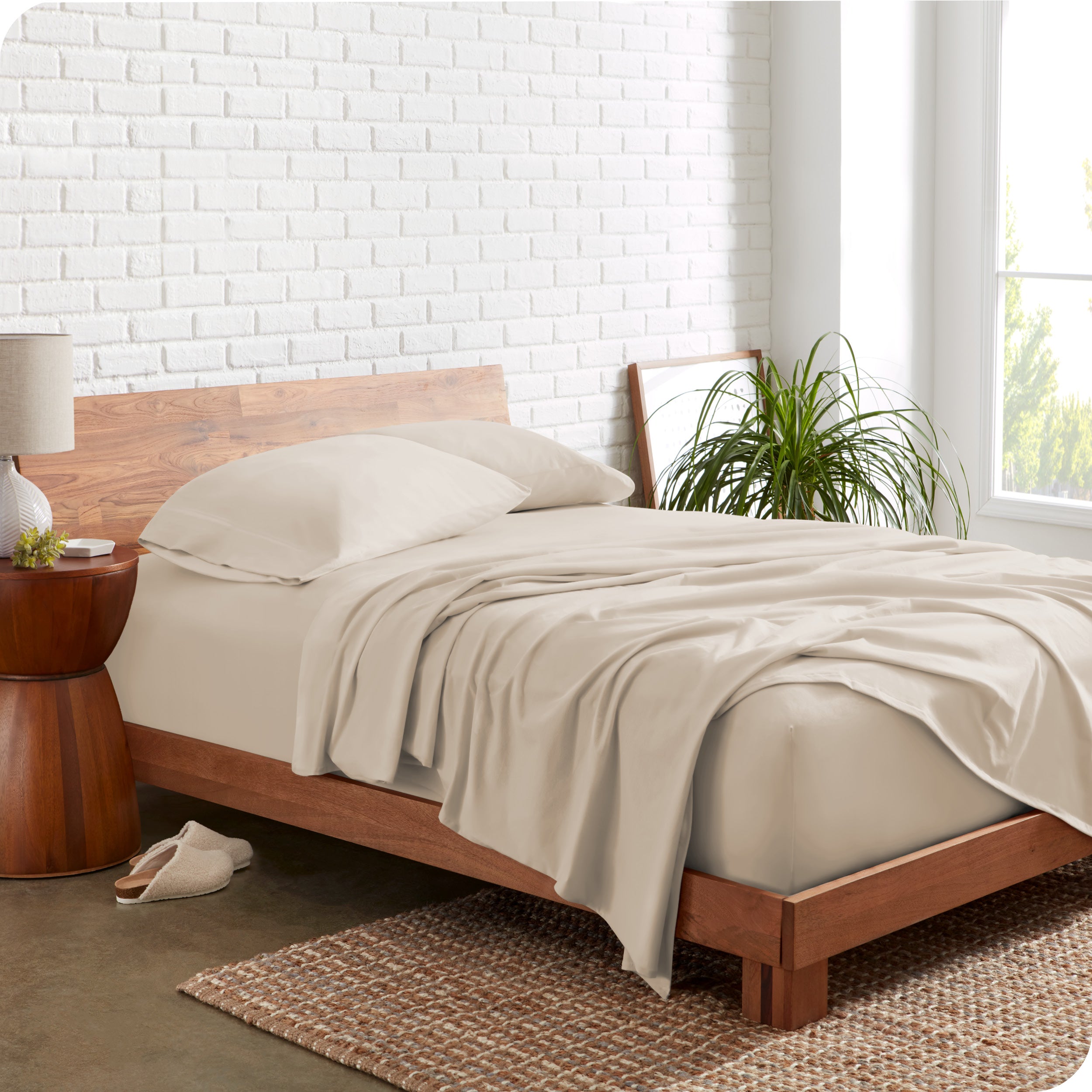 Organic jersey sheets on a bed with a brick wall behind the headboard