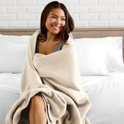A woman sitting at the end of a bed with a fleece blanket wrapped around her shoulders