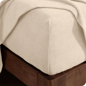 Corner of the bed with a fitted sheet on the mattress and a flat sheet draped over the side and end