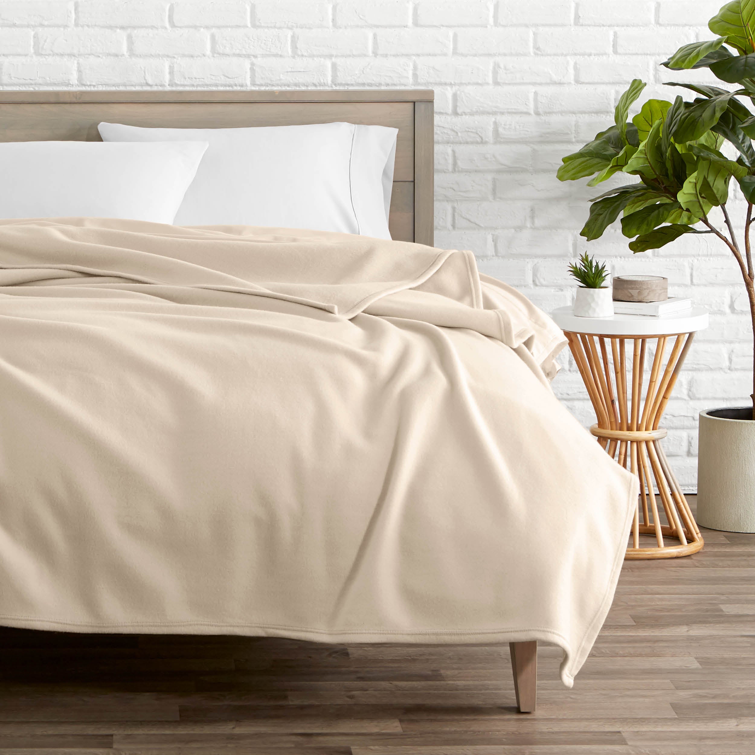 A polar fleece blanket on a bed next to a table and a large plant