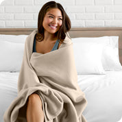 A woman sitting at the end of a bed with a fleece blanket wrapped around her shoulders