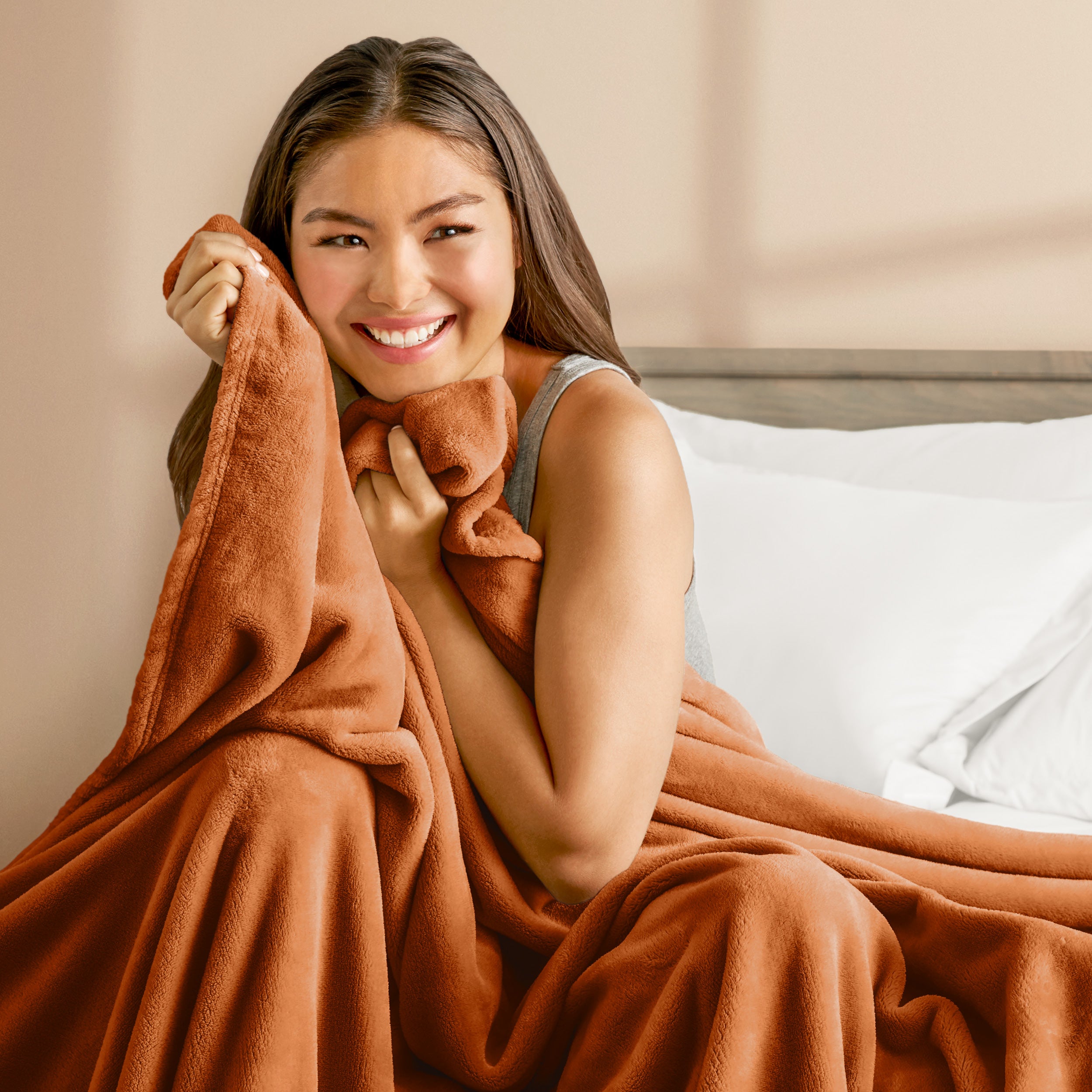 A woman sitting on a bed wrapped in a microplush blanket