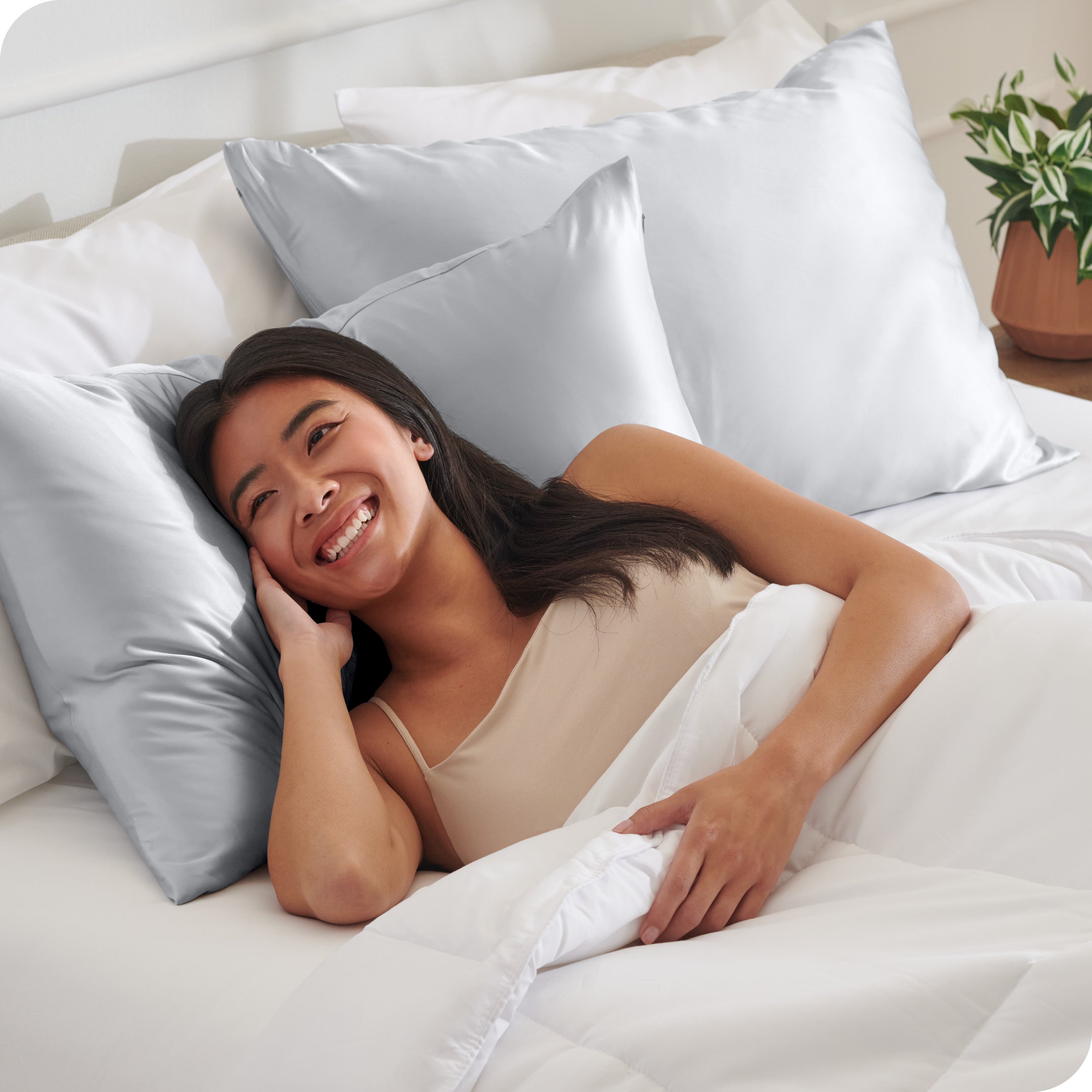 A woman in bed with her head resting on a silk pillowcase covered pillow