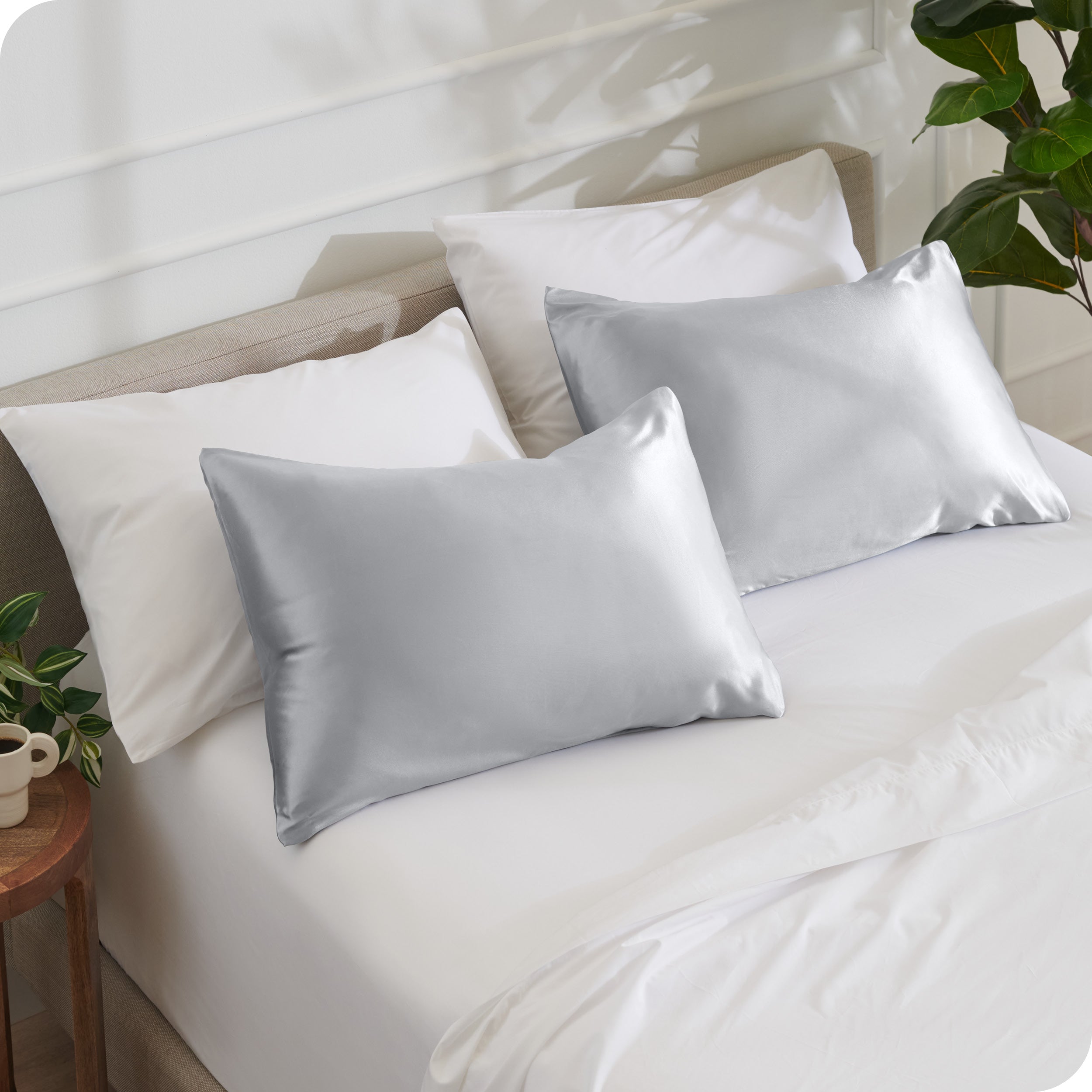 2 satin pillowcases on pillows leaning against other pillows on a bed