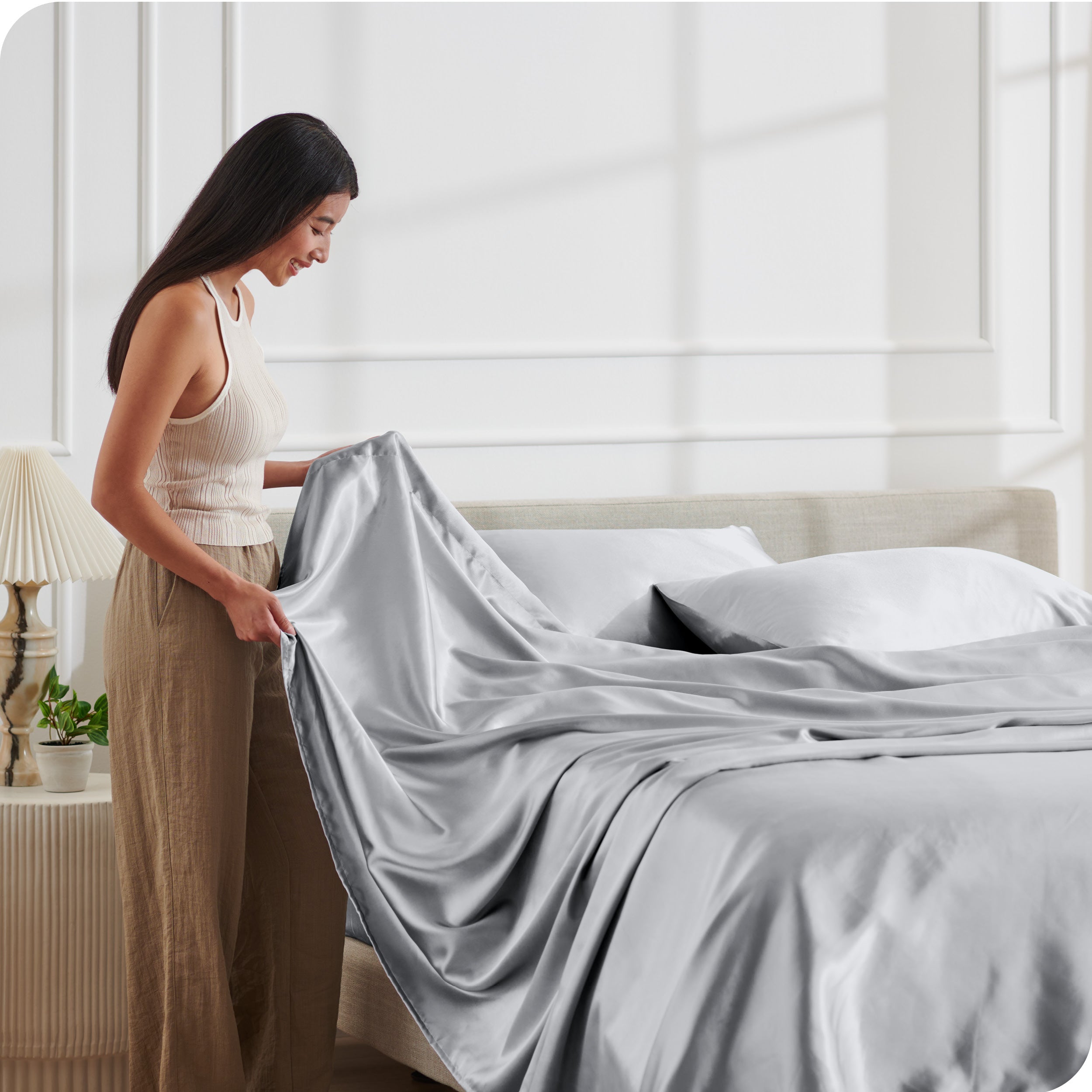 A woman making a bed with satin sheets