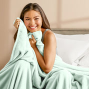 A woman sitting on a bed wrapped in a microplush blanket