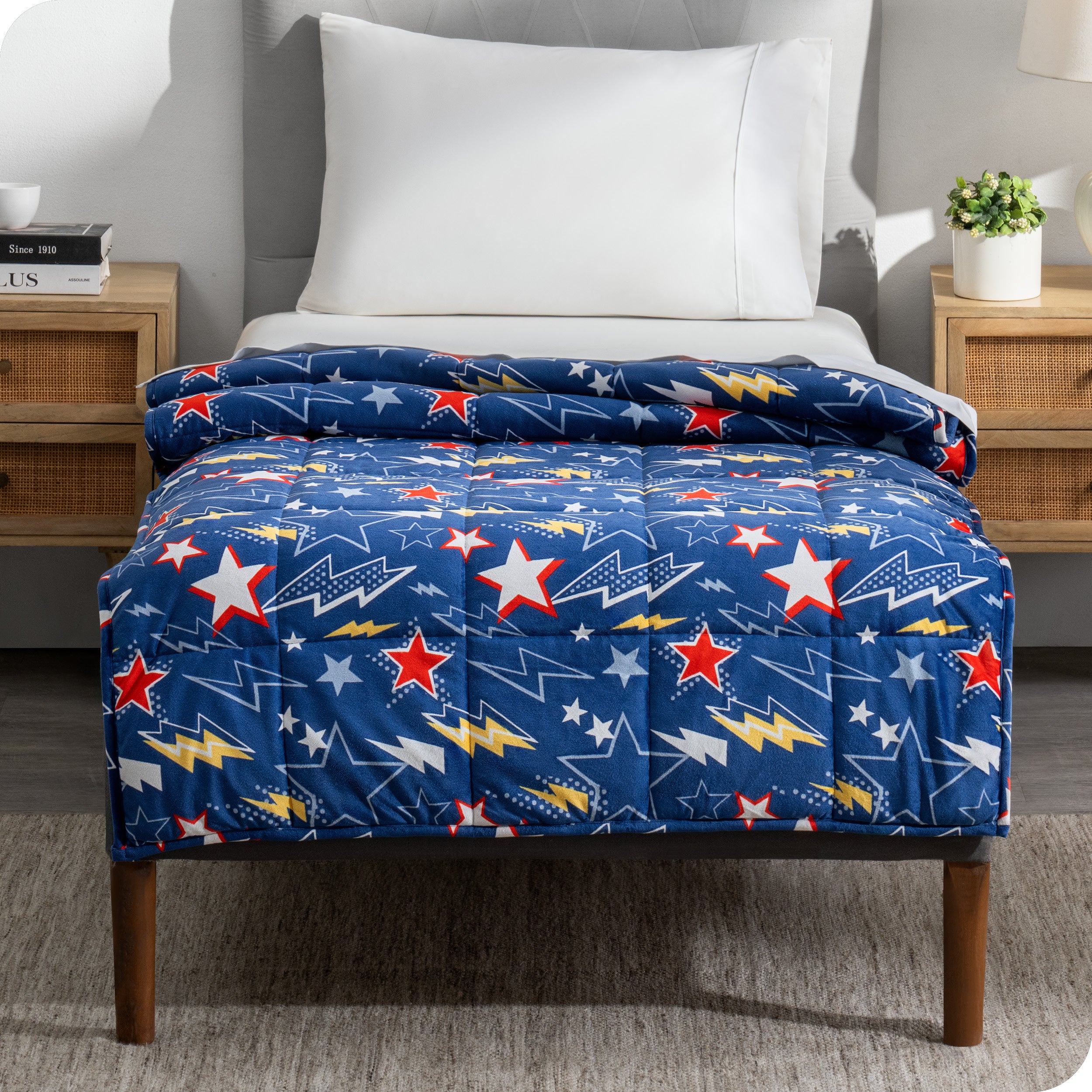 A printed weighted blanket hanging off the end of a twin size bed