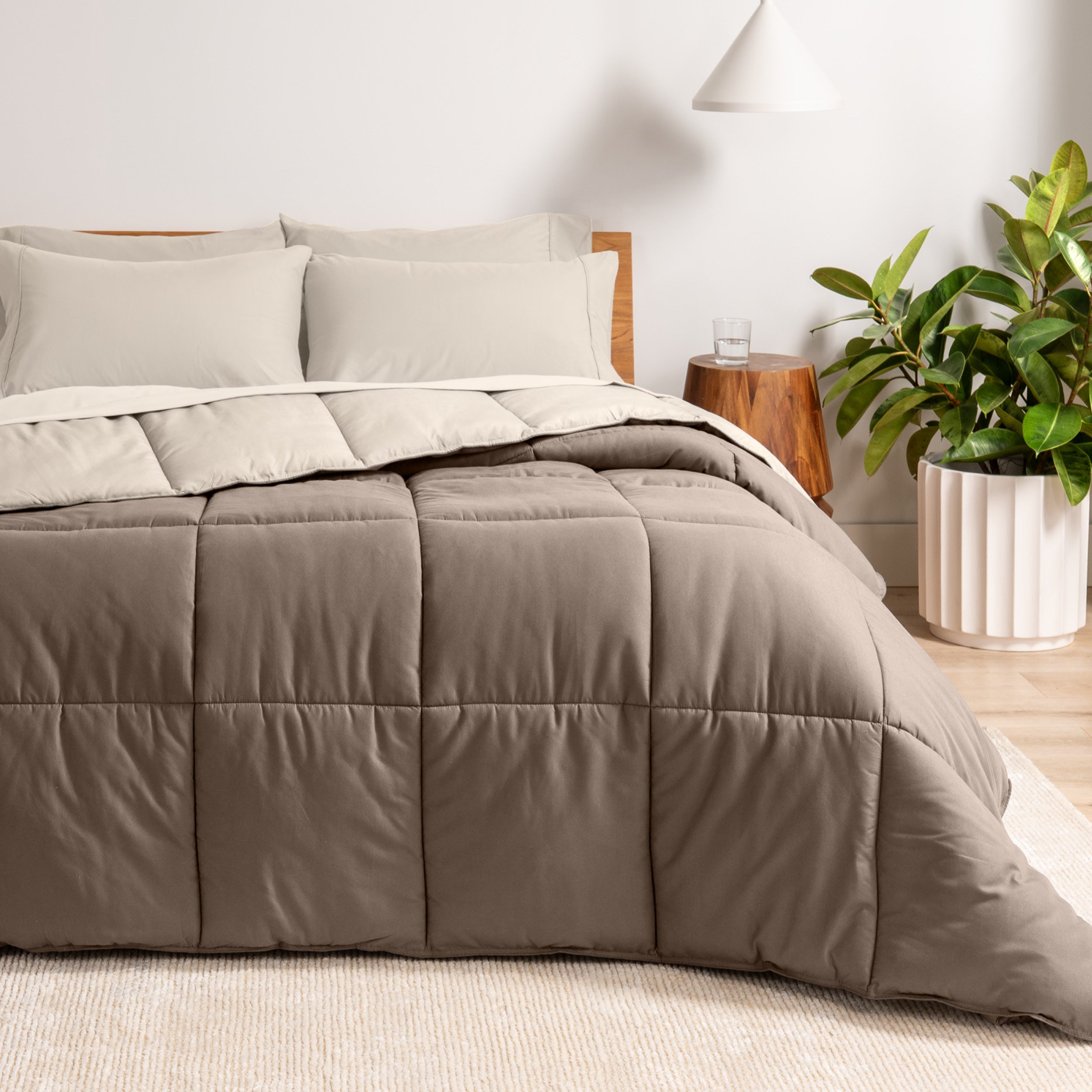A wooden bed frame with a reversible comforter and sheet set on the mattress in a bright warm room.